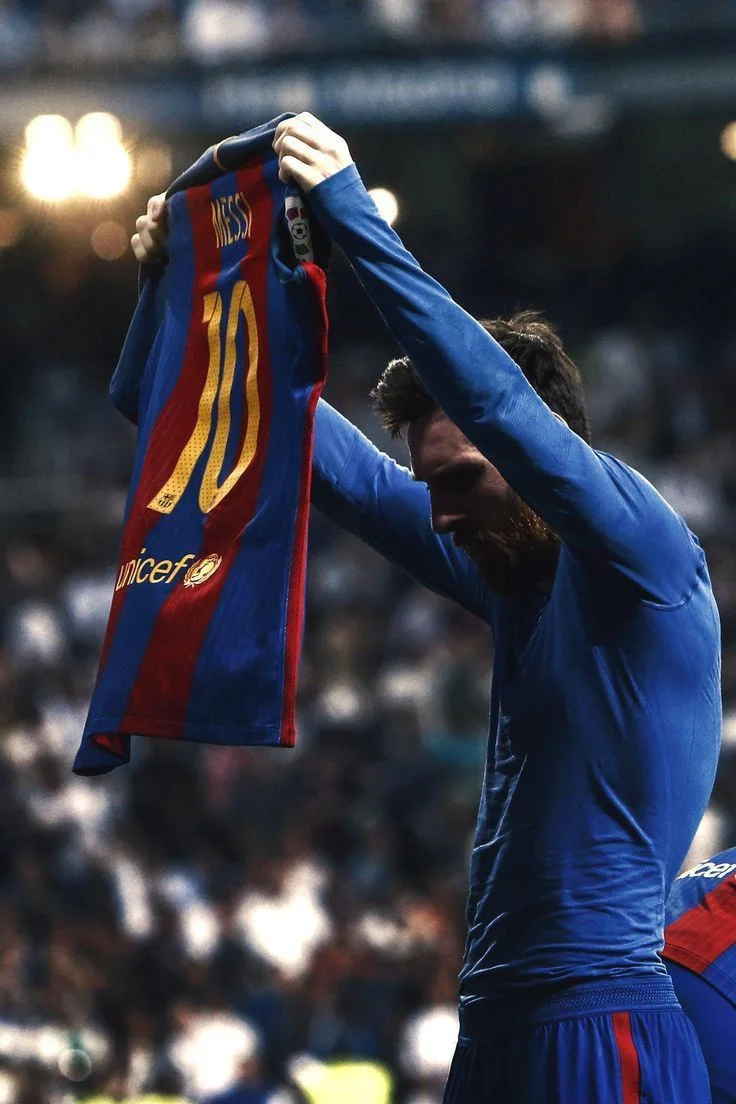 Footballer holding up a blue and red striped jersey with 'MESSI' and number '10' in gold