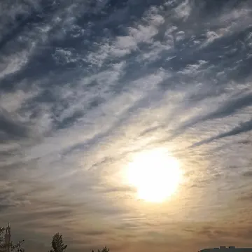 Sunlight breaks through textured clouds over urban skyline and trees at dawn or dusk