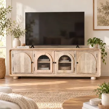 Light wood TV console with arched doors in sunlit living room with plants and woven rug