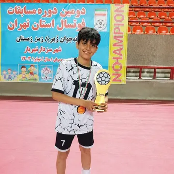Young boy in soccer uniform holding golden trophy in indoor sports arena