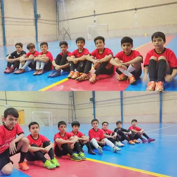 Group of young soccer players sitting on an indoor court wearing red jerseys and colorful cleats