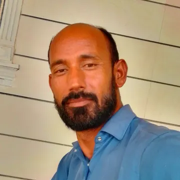 Man with dark beard and bald head wearing blue shirt standing near paneled wall