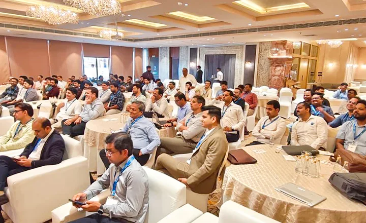 Men in business attire seated in a conference hall listening to a presentation