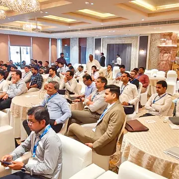 Men in business attire seated in a conference hall listening to a presentation