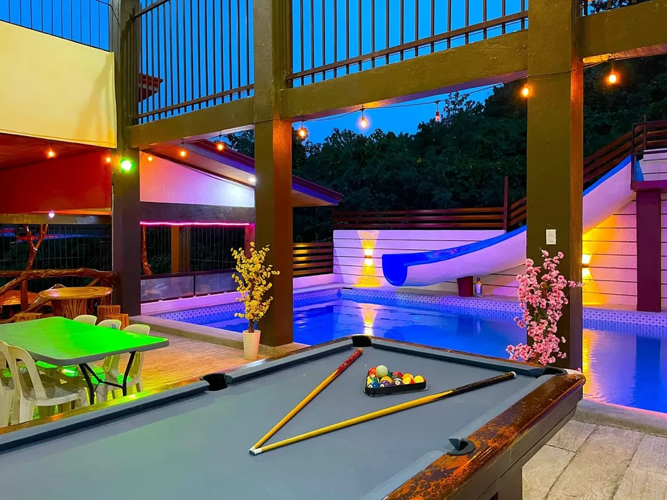 Pool table beside a lit pool with slide at dusk