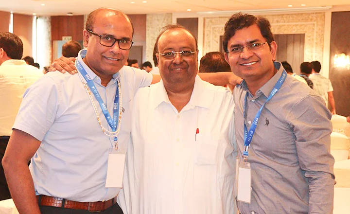 Three men in glasses and lanyards smiling at a conference event