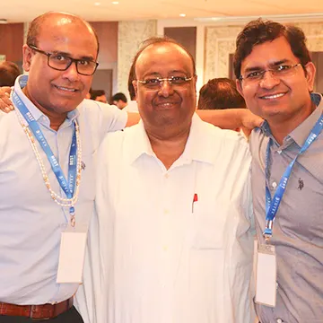 Three men in glasses and lanyards smiling at a conference event