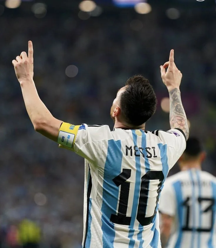 Soccer player wearing Argentina jersey number 10 pointing upward in celebration at a stadium