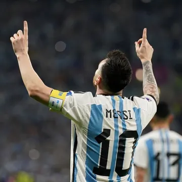 Soccer player wearing Argentina jersey number 10 pointing upward in celebration at a stadium