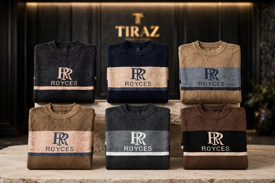 Six folded Royces brand sweaters with logo stripes arranged on a stone pedestal in a luxury retail setting