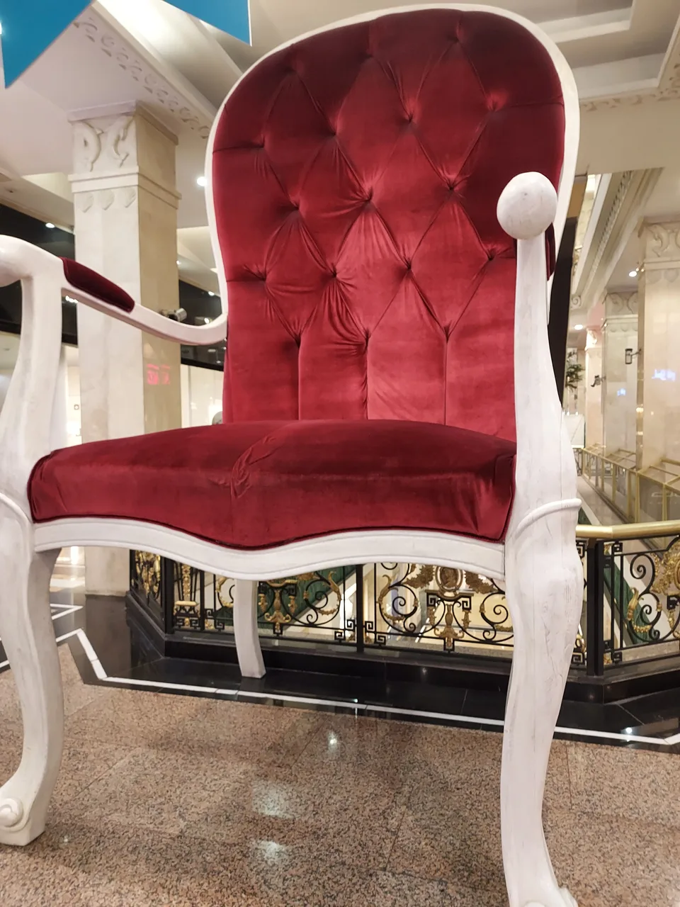 Red velvet tufted chair with white frame in a luxurious marble lobby with gold railings