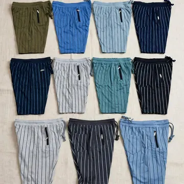 Ten pairs of striped shorts in various colors neatly arranged on a beige fabric surface