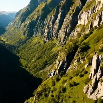 A high-angle view of a steep, rocky mountain valley with green vegetation under a clear blue sky