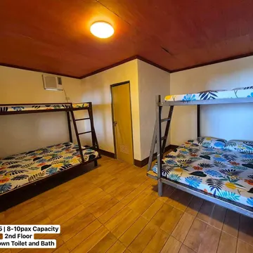 Two metal bunk beds with tropical leaf sheets in a wooden-floored guest room with yellow walls and ceiling light