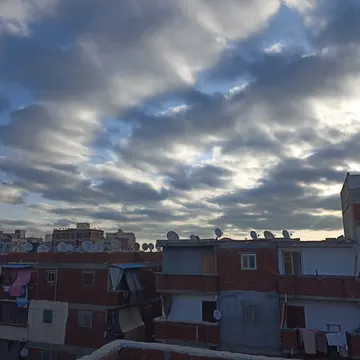 Urban rooftops with satellite dishes and laundry under a dramatic cloudy sky at dusk
