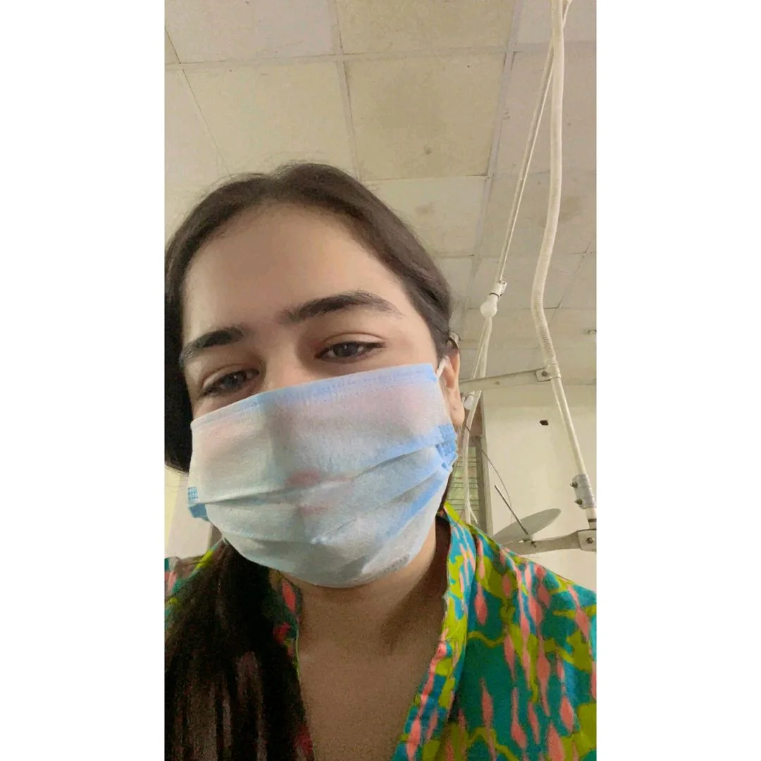 Young woman wearing a blue surgical mask and colorful shirt indoors