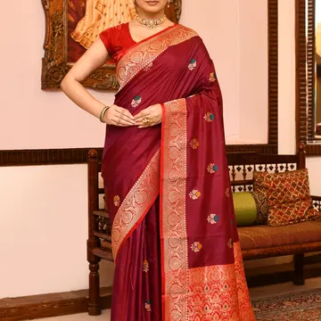 Woman wearing ornate maroon silk saree with gold embroidery standing in traditional Indian room
