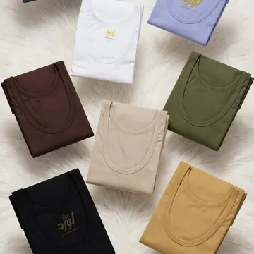 Seven folded t-shirts in various colors are arranged on a white furry surface, with a branded box and a 'TIRAZ STORE' plaque visible