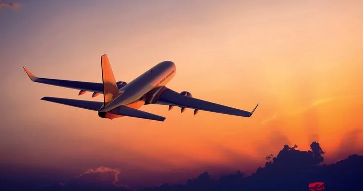 An airplane flying against a colorful sunset sky with clouds below
