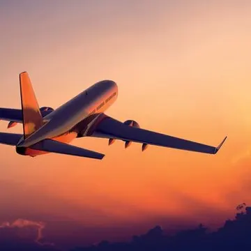 An airplane flying against a colorful sunset sky with clouds below