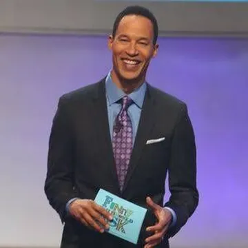 Man in suit holding Family Feud card on TV game show set