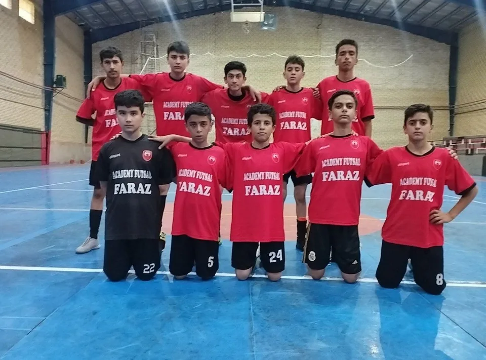 Youth futsal team in red and black uniforms posing on blue indoor court