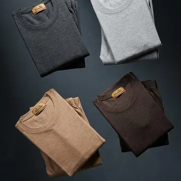Four folded TIRAZ brand t-shirts in gray brown and tan floating in a dark studio setting