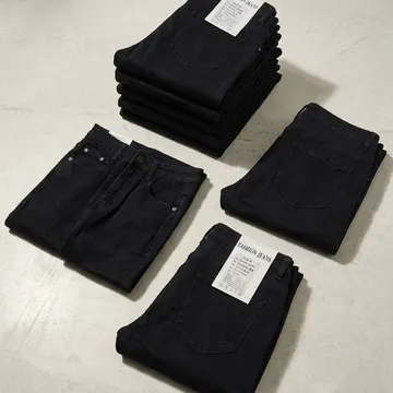 Neatly folded dark jeans with tags on a gray concrete surface