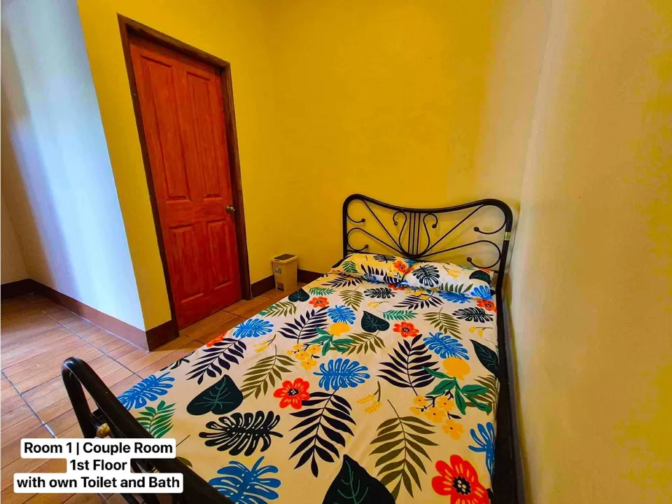 A bedroom with yellow walls and a bed covered in a colorful tropical floral patterned sheet
