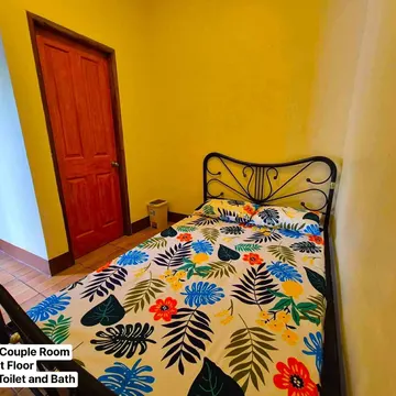A bedroom with yellow walls and a bed covered in a colorful tropical floral patterned sheet