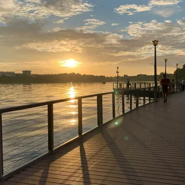 Sunset over a wooden boardwalk with people walking and water reflecting golden light