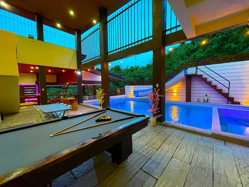 Pool table beside a blue lit pool with slide and stairs at twilight