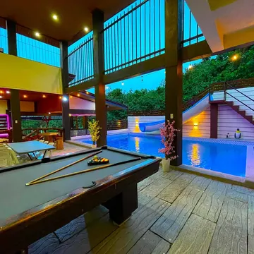 Pool table beside a blue lit pool with slide and stairs at twilight