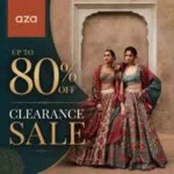 Two women wearing colorful embroidered lehengas standing in front of a stone archway during a clearance sale