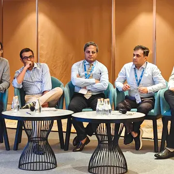 Five men in business attire seated at a conference panel with microphones and water bottles