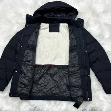 A black puffer jacket with a white fleece lining is laid open on a white fluffy rug, showing its quilted interior and zipper details