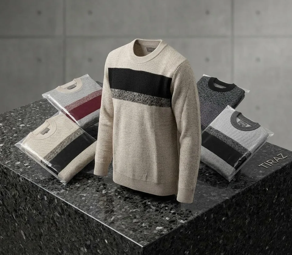 Beige sweater with black stripe displayed on granite pedestal with packaged sweaters nearby