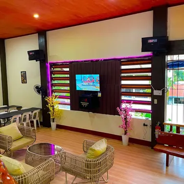Cozy lounge with wicker chairs yellow cushions and purple neon lights around a karaoke screen