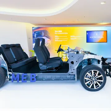 Exposed Volkswagen MEB electric vehicle chassis with black seats and orange wiring on display