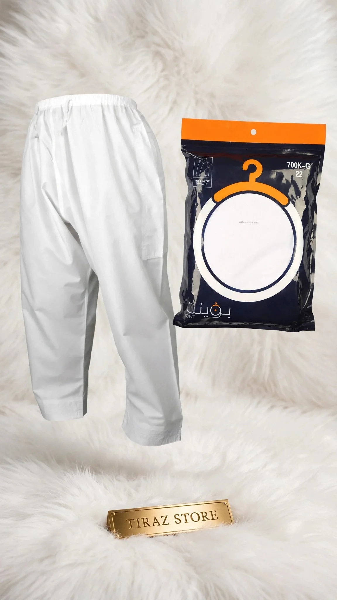 A pair of white pants and a packaged hanger are displayed on a white furry surface, with a gold plaque reading 'TIRAZ STORE' in front