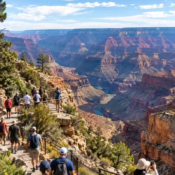 Hikers walking on a stone path overlooking the Grand Canyon with red rock formations and a river below