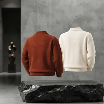 Two ribbed knit sweaters in rust and cream hang suspended above a black marble slab against a gray concrete wall