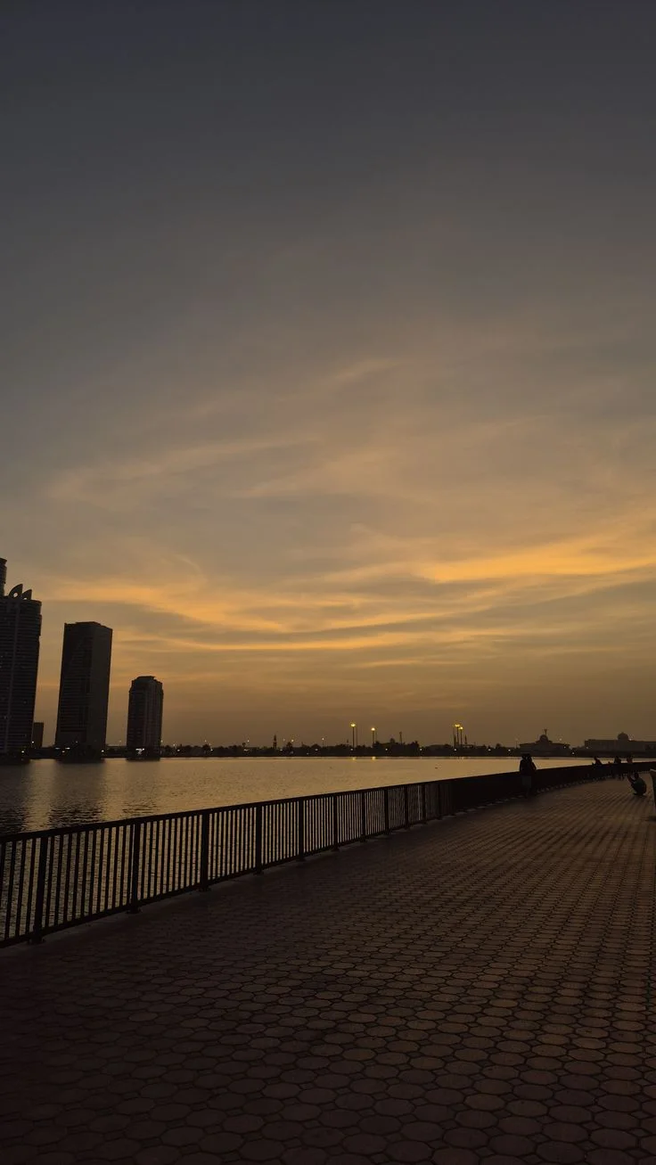 Silhouetted city skyline at sunset reflected on water beside a hexagonal tiled walkway