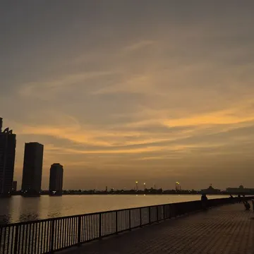 Silhouetted city skyline at sunset reflected on water beside a hexagonal tiled walkway