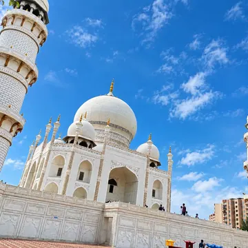 White marble mosque with domes and minarets under a bright blue sky with clouds