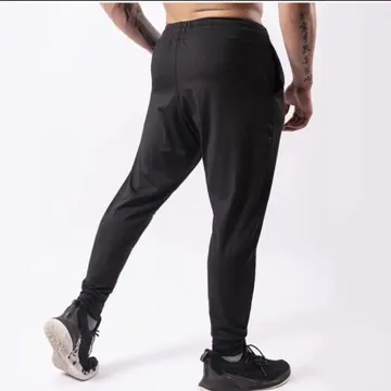 Person wearing black joggers and sneakers with tattoos on arms standing in studio